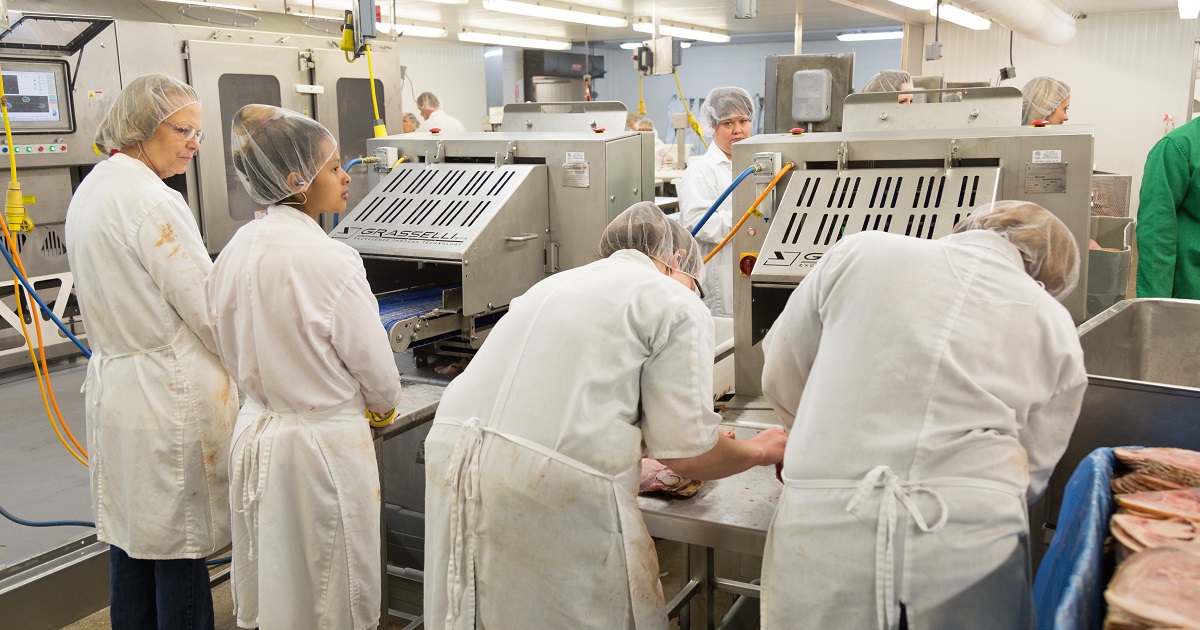 Meat processing employees use safe slicing equipment