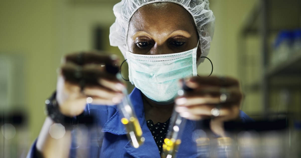 Lab worker holds two vials while wearing a mask