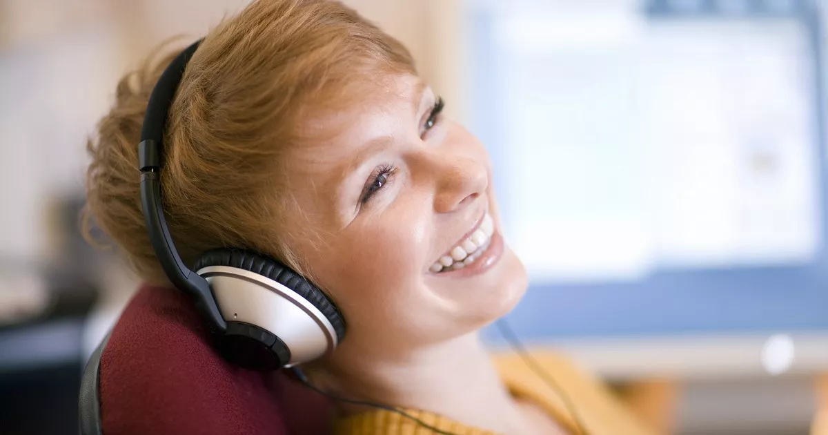 Woman wearing headphones smiles in front of computer screen